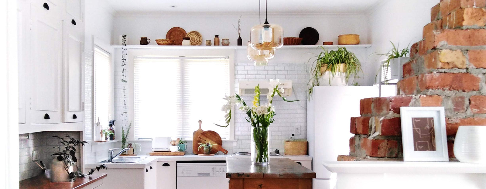 White farmhouse style kitchen with subway peel and stick tiles and white vinyl wrapped bench top. Red brick fireplace to the right