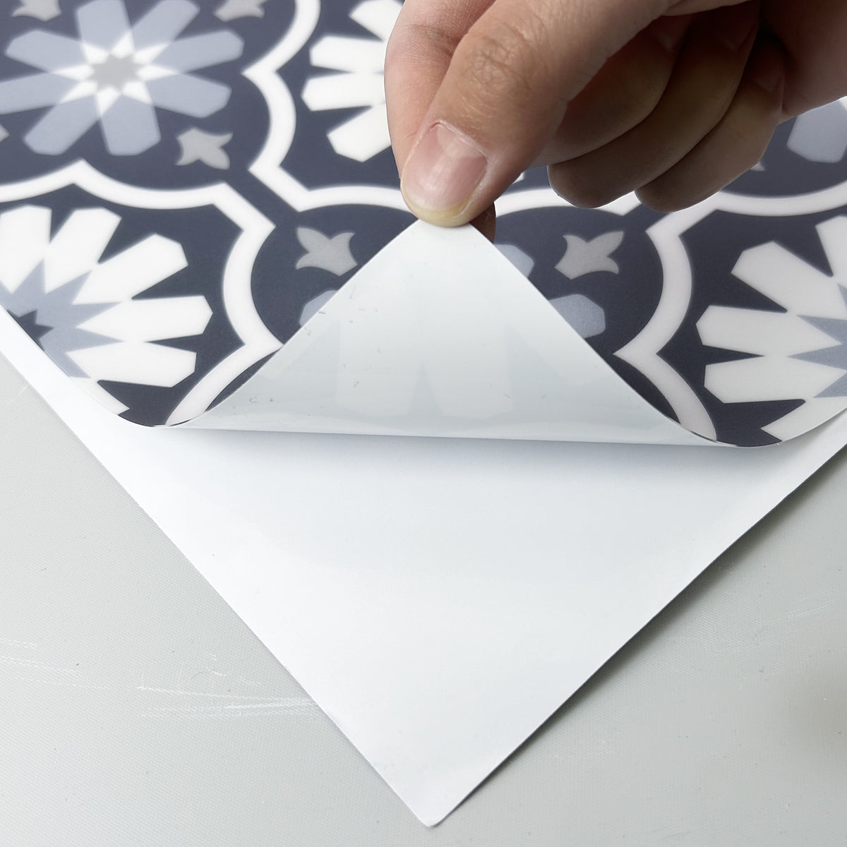 Hand peeling back a self-adhesive blue floral floor tile