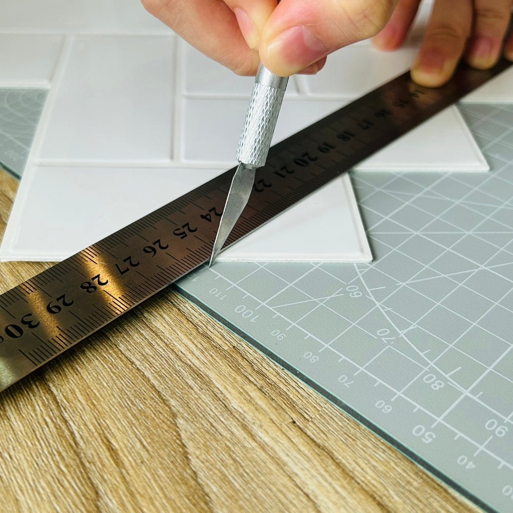 Self-adhesive tiles being cut on self-healing craft mat with utility knife and metal ruler