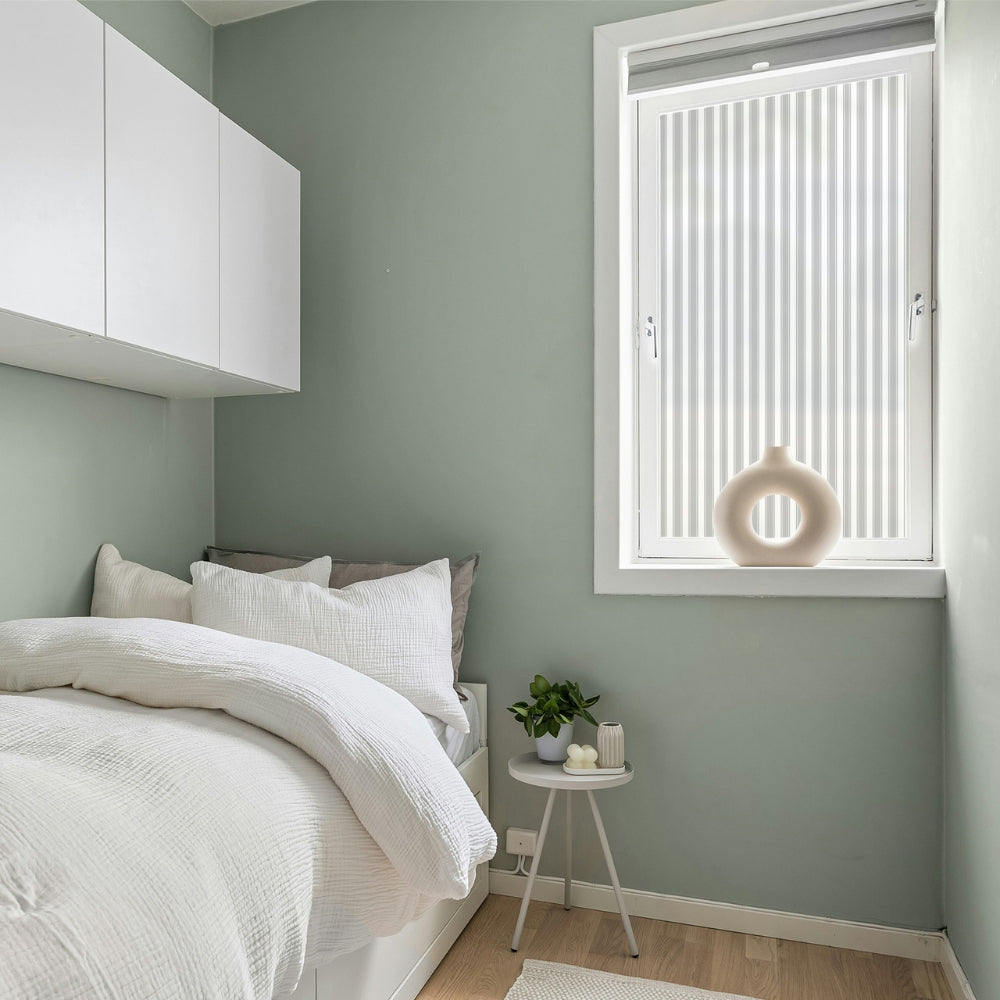 Modern bedroom with green walls, white furniture, and a small round table with decor items and reeded window film covered window.