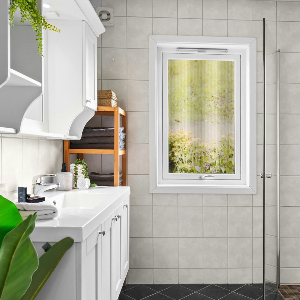 Modern bathroom with white cabinets, a window with fluted window film, and a shower area.