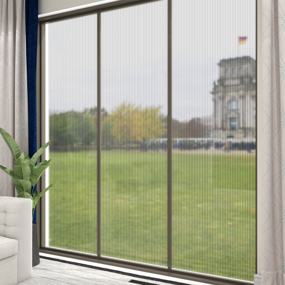 Window with reeded window film with a view of a green field and building, featuring a plant and part of a sofa.