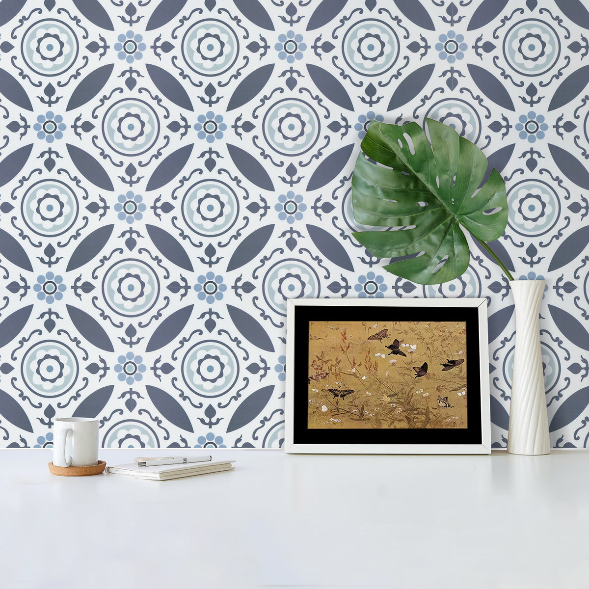 Decorative wall with patterned wall tiles, framed artwork, and a plant on a white surface.