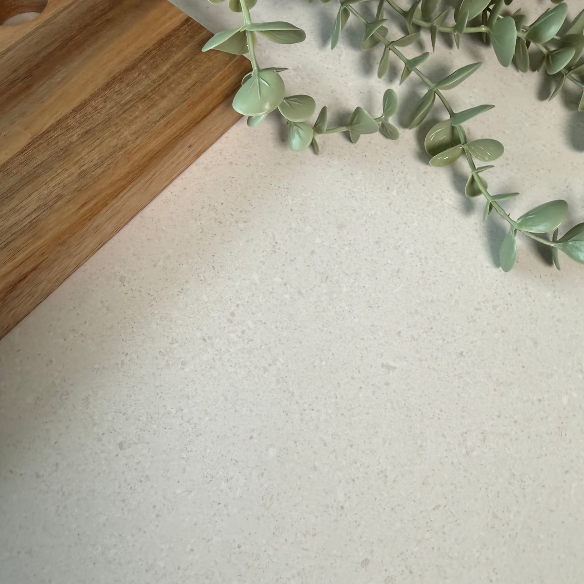 Close-up of a greige countertop with a wooden cutting board and green leaves.