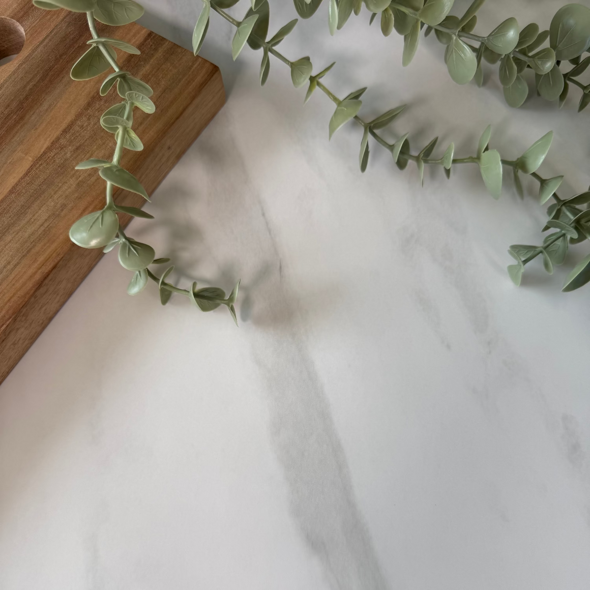 Green leaves on a white marble surface with a wooden cutting board