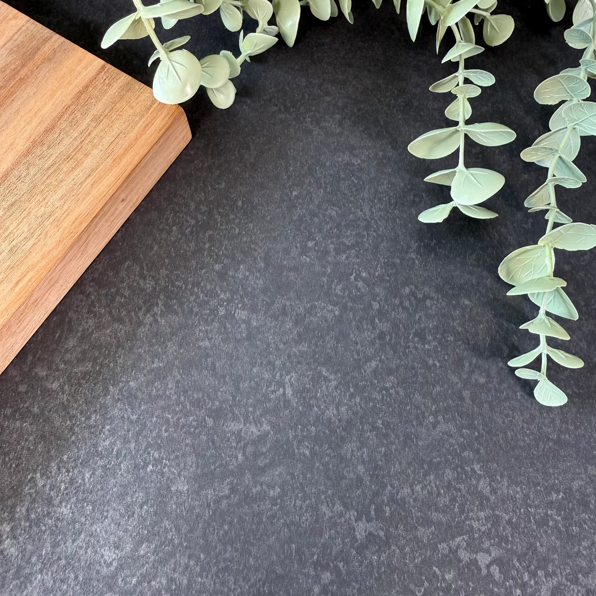 Dark grey vinyl wrapped countertop with a wooden cutting board and green leaves.