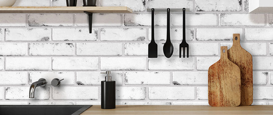 White and grey brick vinyl wall tiles in a kitchen with wooden bench top and black utensils hanging down on wall