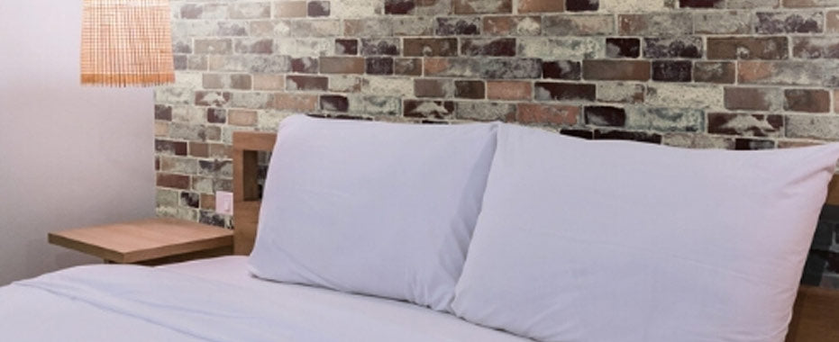 red old brick waterproof wallpaper behind a bed with two large white pillows and a wooden side table to the left