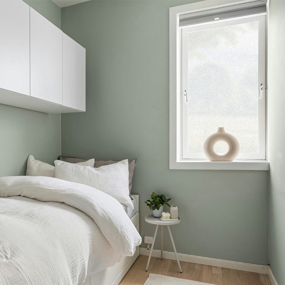 Modern bedroom with green walls, white furniture, and a small round table with decor items.
