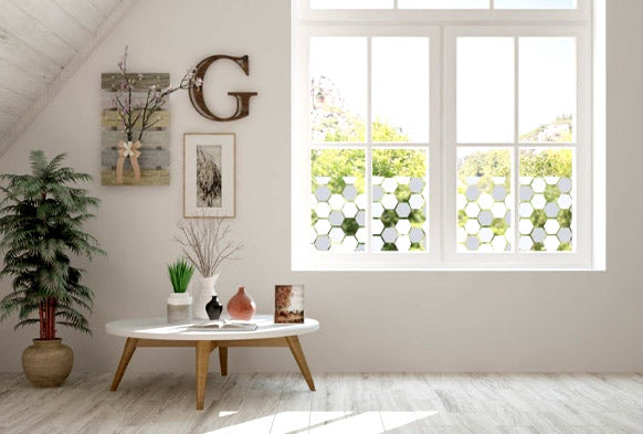 Grey hexagon window film on large white window in airy top room with small table and plant to the left