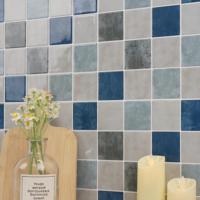 Decorative setting with a vase, croissant, and candles against a tiled checkered blue and grey wall.