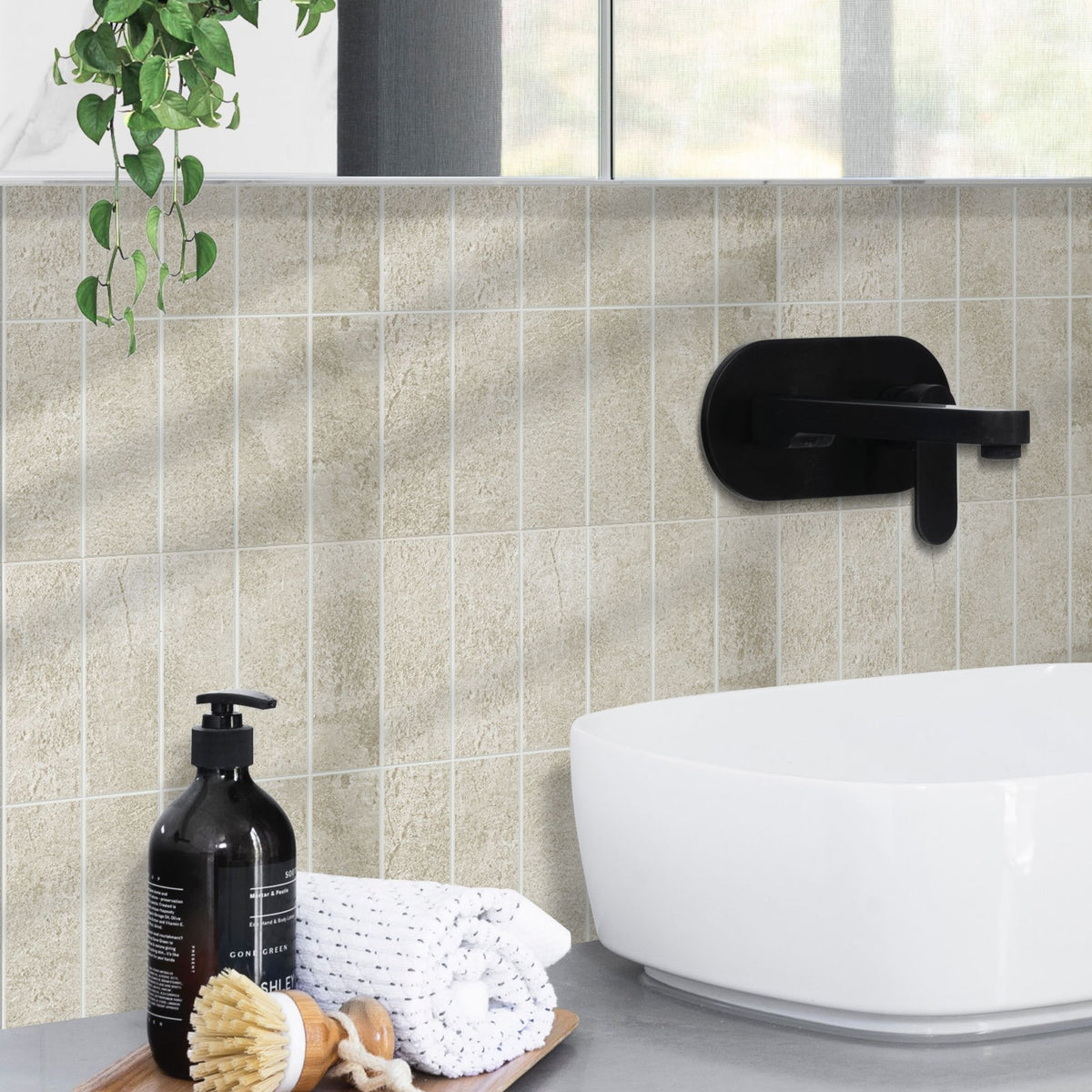 A white bathroom basin with a black tap, the backsplash is textured beige stacked subway tiles and a tray with soap, brush and towel.