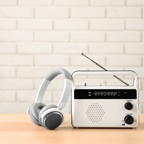 White radio to the right and grey headphones leaning against it on birch benchtop with white brick backdrop