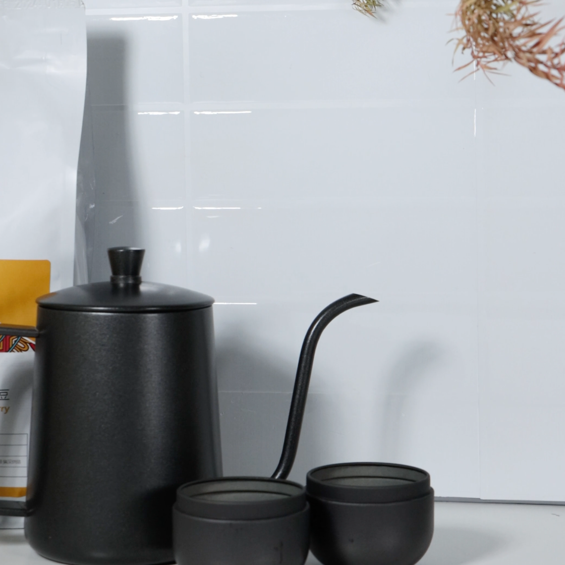 Black ceramic teapot and cups on a white surface with a tiled wall background