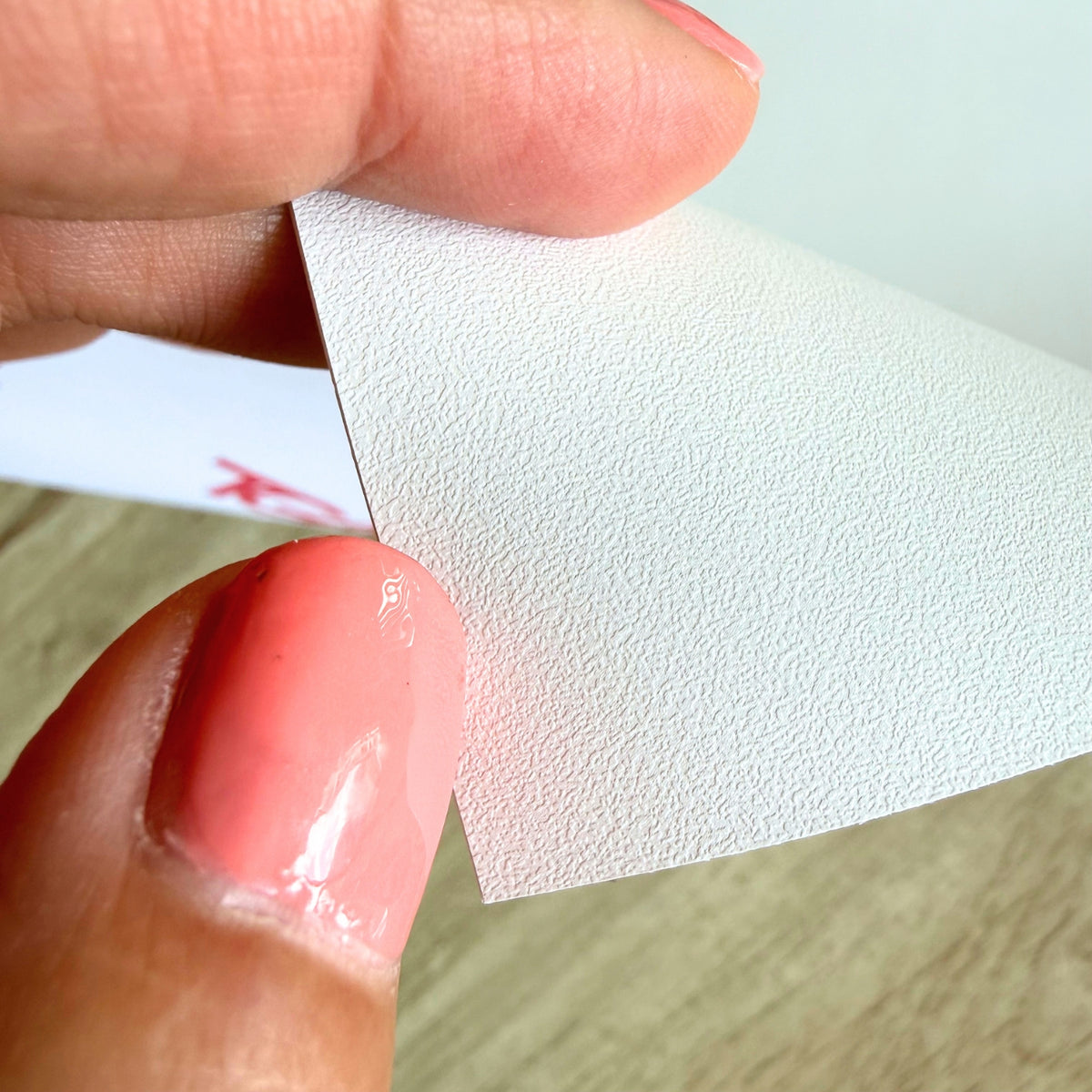 A close-up of a hand holding a textured white adhesive vinyl, showing the surface detail and satin finish.