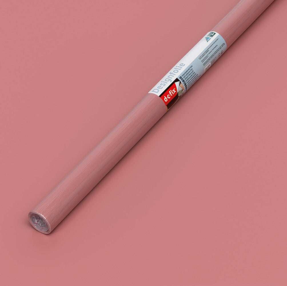 A roll of dusty rose pink adhesive vinyl with a white and red label, placed diagonally on a matching dusty rose background.