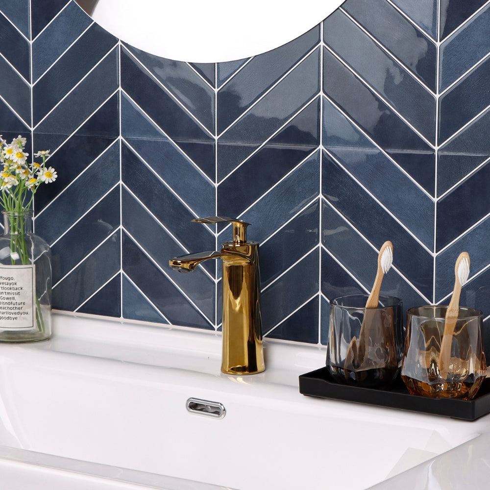 Bathroom sink area with gold faucet, toothbrushes, and a vase against a blue tiled wall.