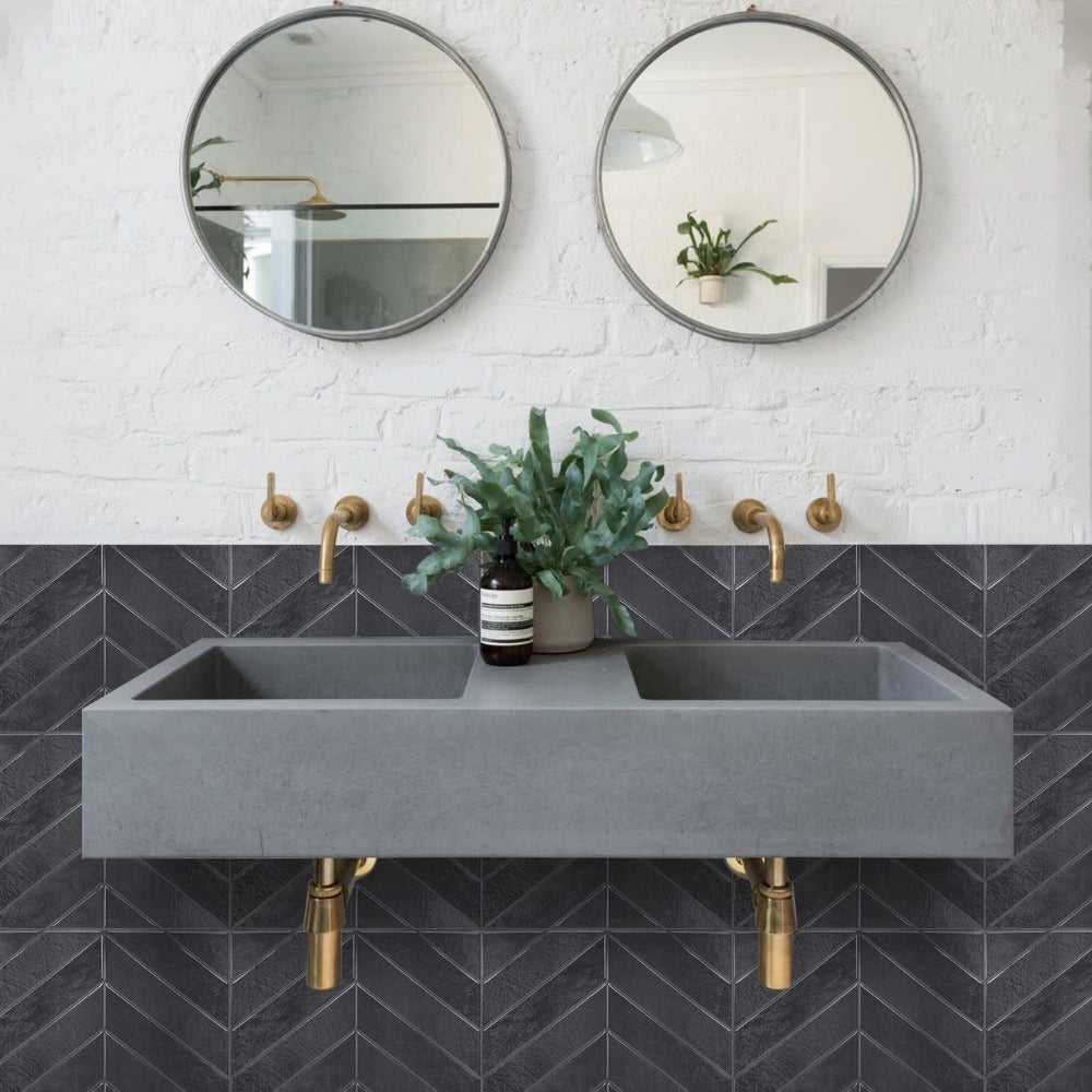 Bathroom with grey concrete sink, gold faucets, and round mirrors on a white brick and grey chevron wall.