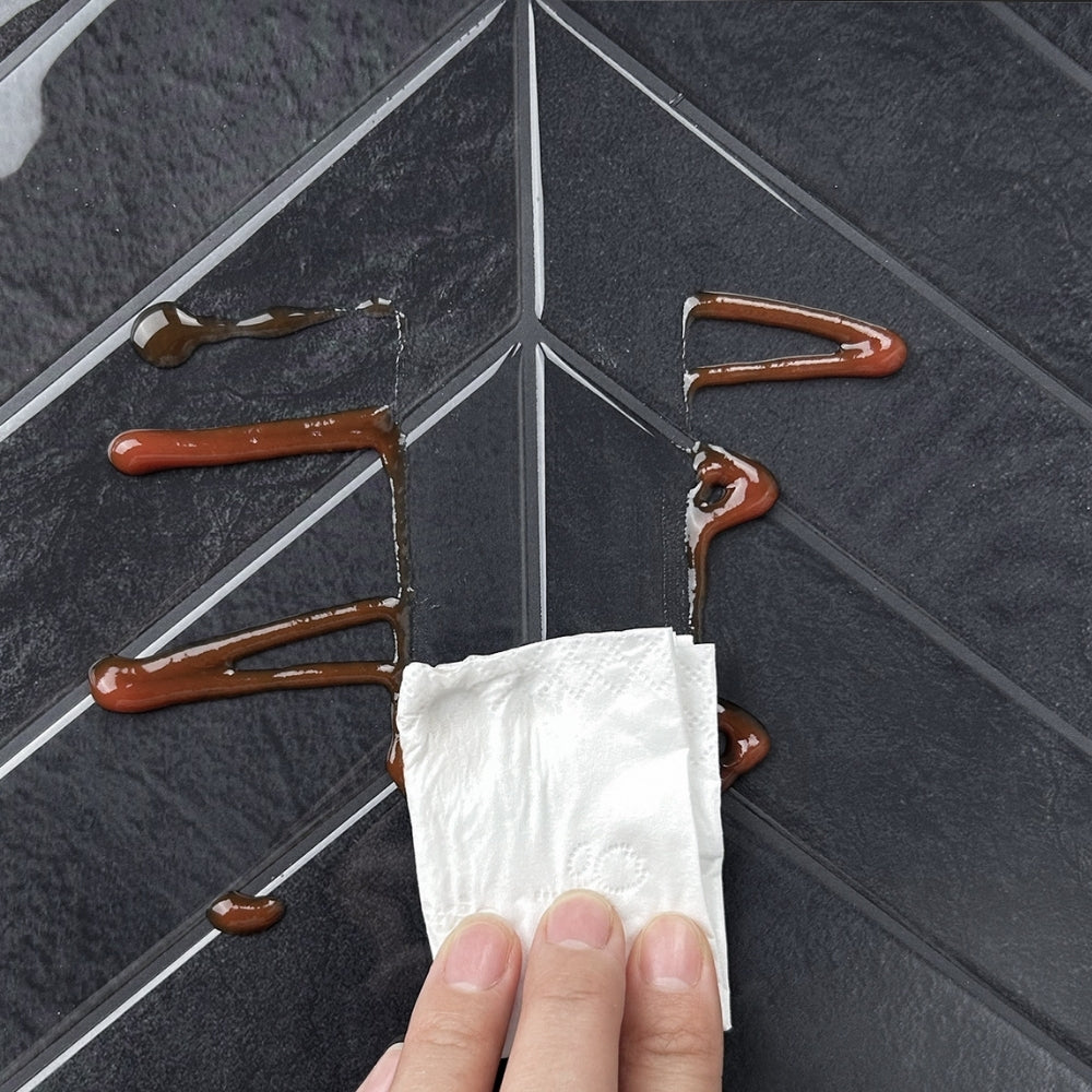 Hand using a paper towel to clean up sauce on a chevron tile.