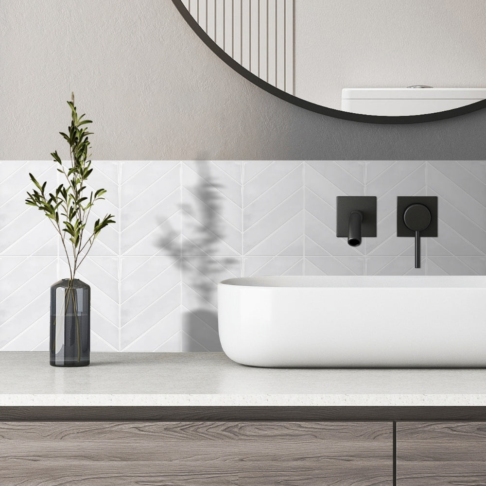 Modern bathroom with a white sinkand off white chevron tiles, black fixtures, and a vase with greenery.