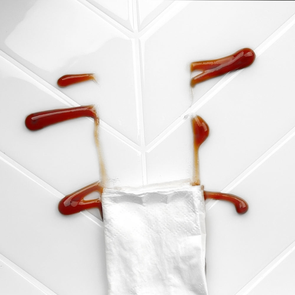 White napkin wiping off tomato sauce from an off white chevron tile