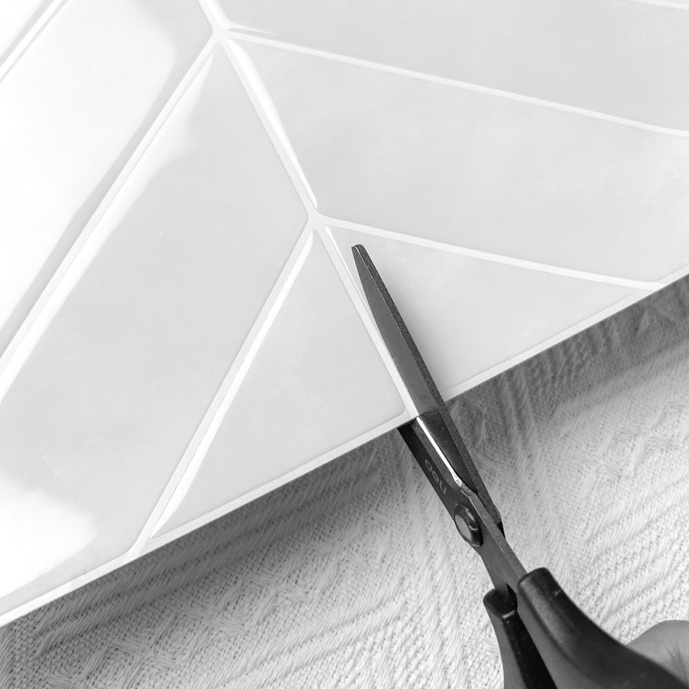 Scissors cutting a chevron off white tile