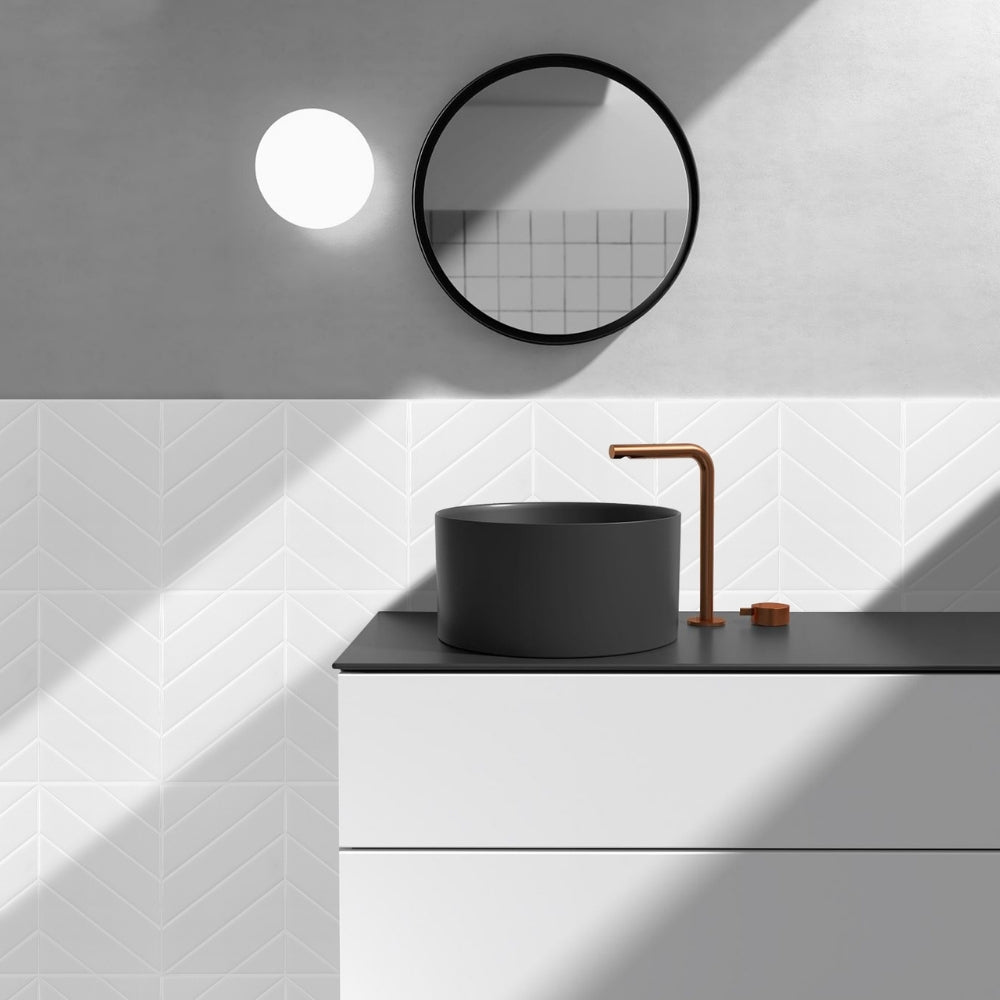 Bathroom with a black sink, bronze faucet, and round mirror on a white tiled wall.