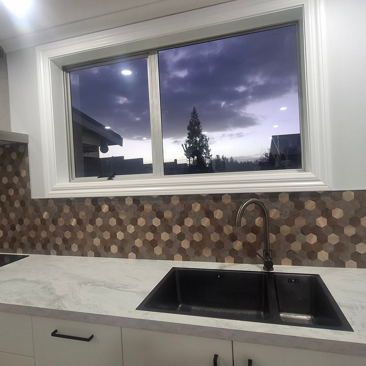 Modern kitchen with a sink, countertop, and window showing a cloudy sky.