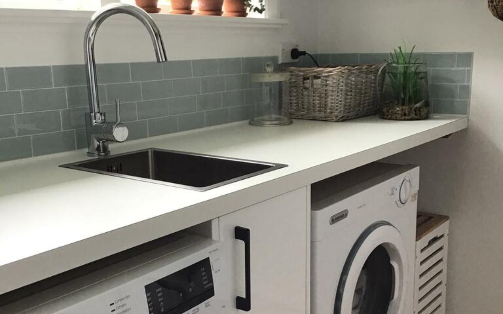 laundry with white countertop, sink, and washing machine below a green tiled wall.