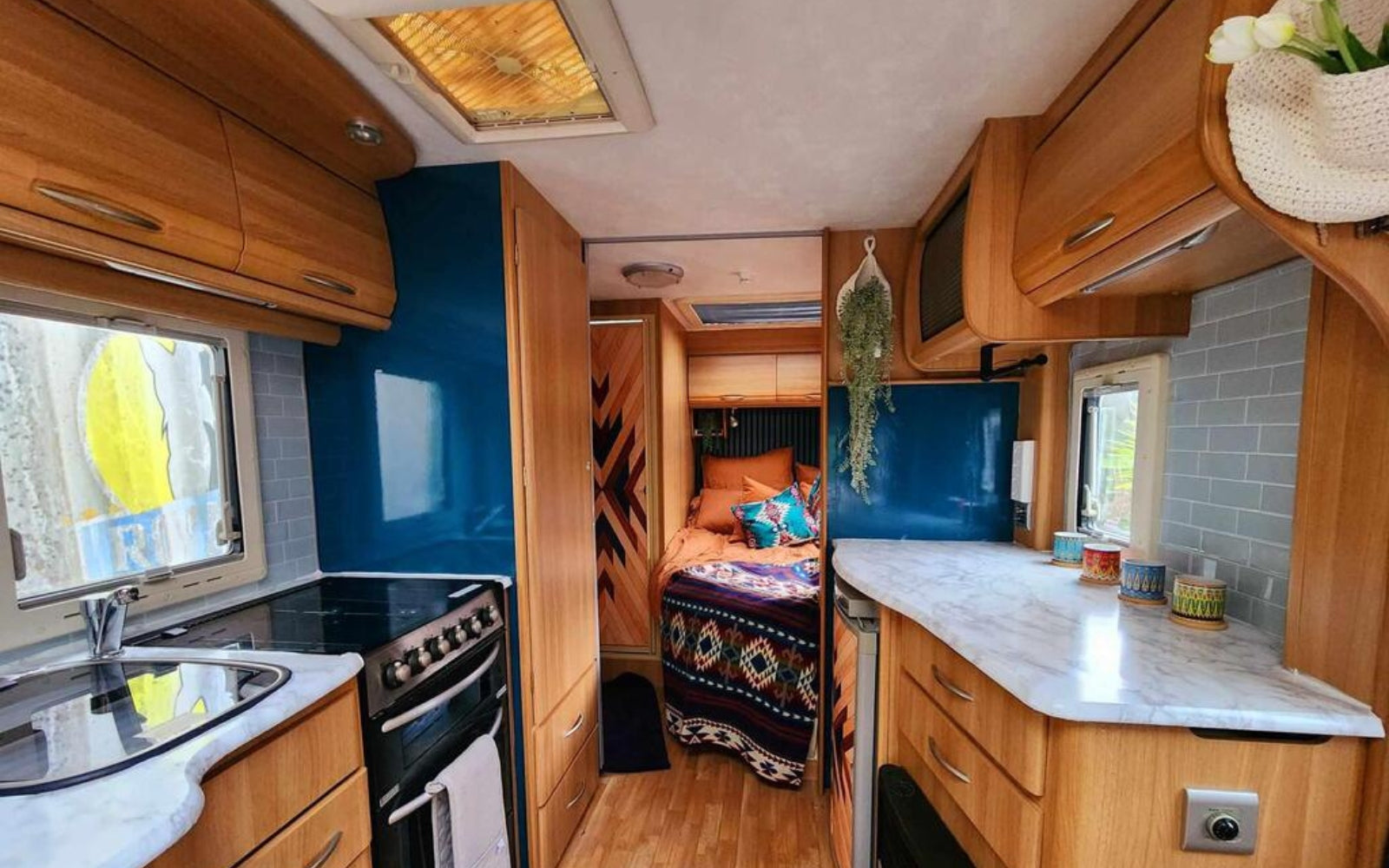 Interior of a compact living space with wooden cabinets, kitchen appliances, and self-adhesive wall tiles splashback.