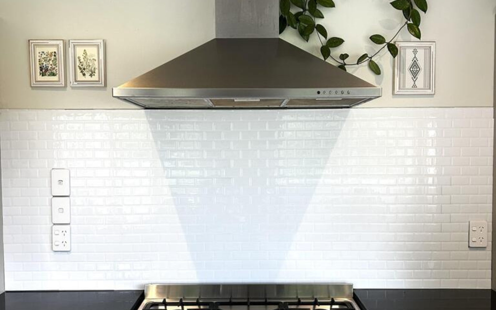 Modern kitchen with stainless steel range hood and white tiled backsplash.