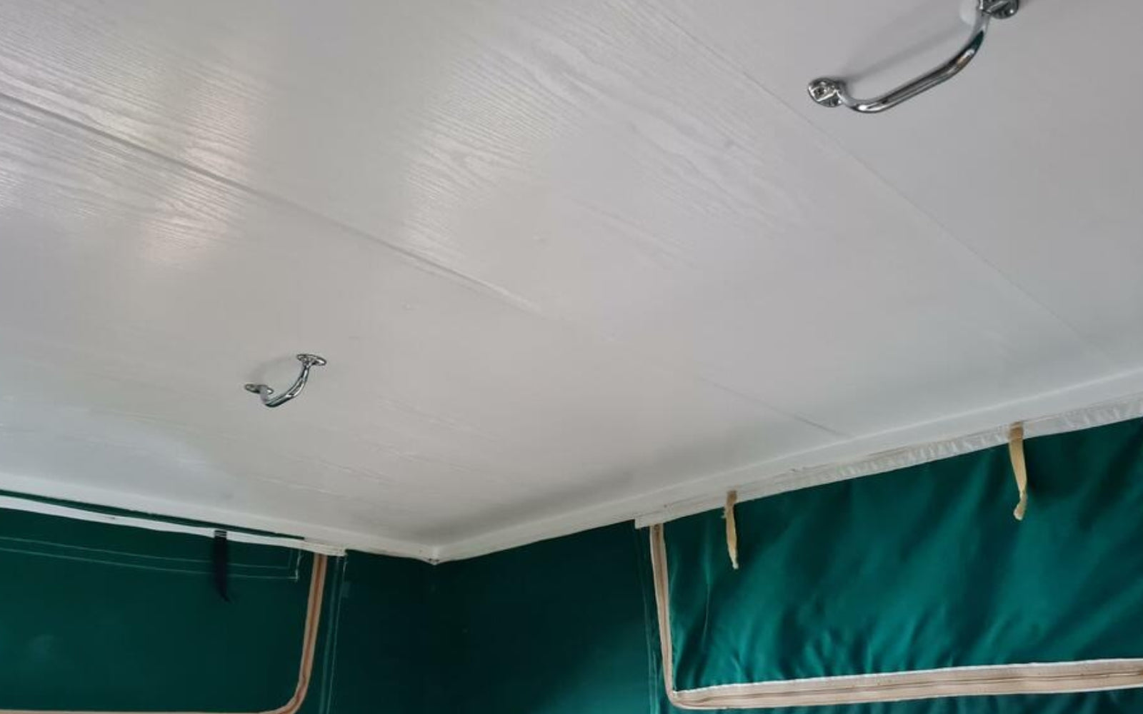Close-up of a white ceiling with hooks and a green fabric surface.