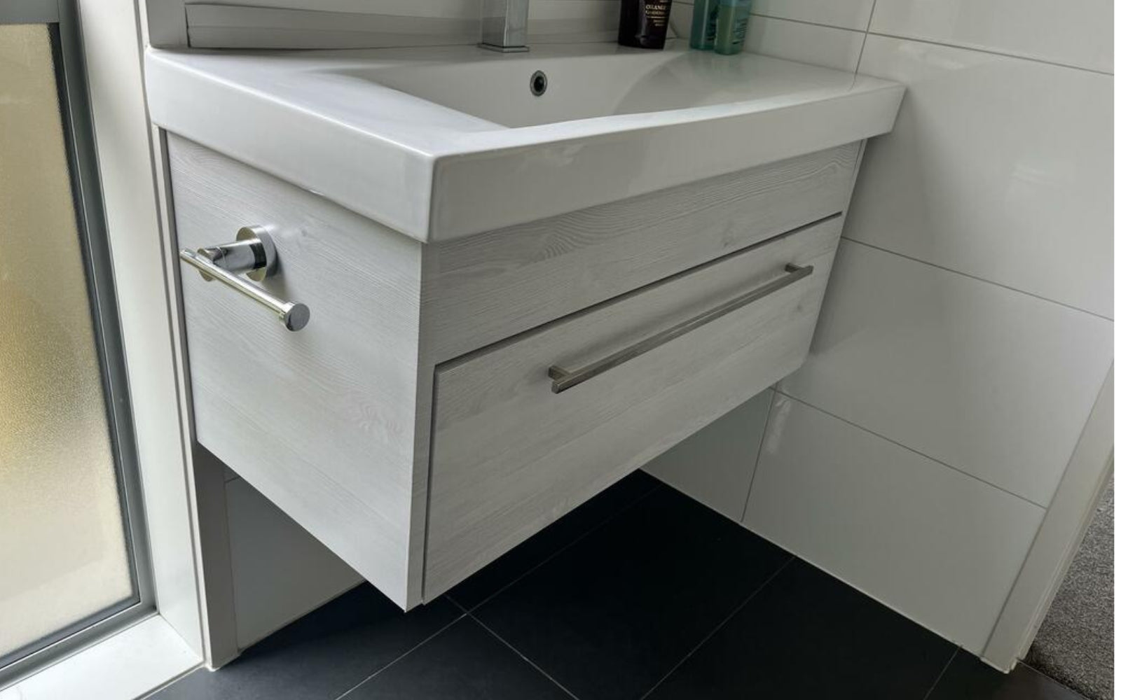 Vinyl wrapped bathroom vanity with sink and drawers in a tiled bathroom setting