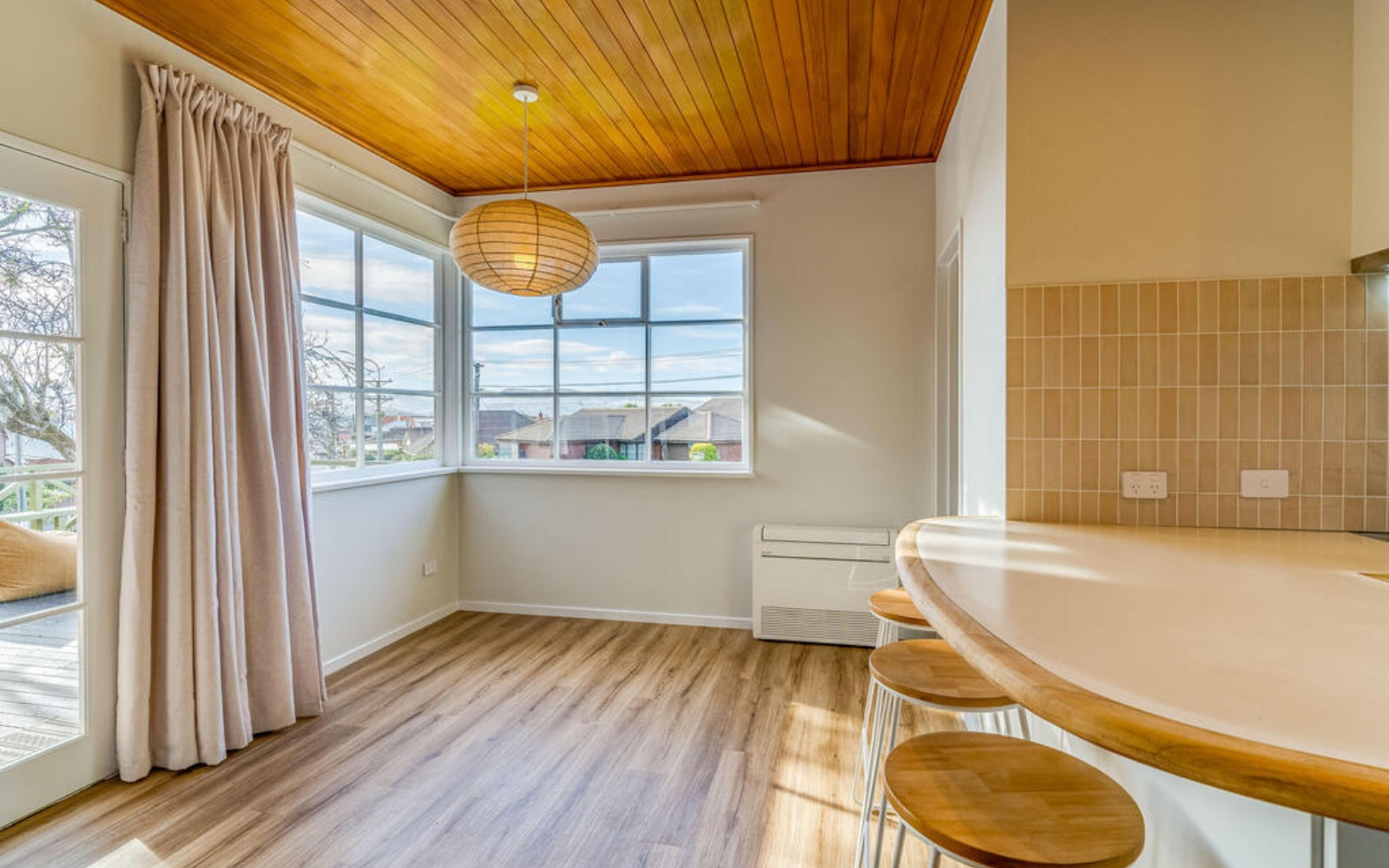 Modern kitchen with wooden ceiling, large window, and bar stools and cream backsplash.