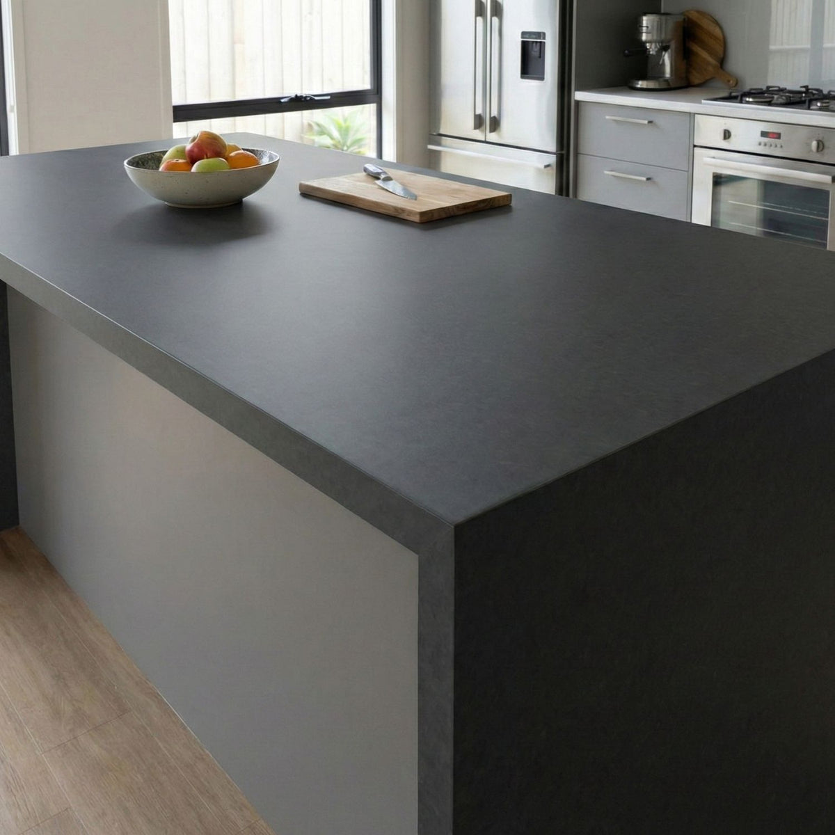 Modern kitchen with a grey island vinyl wrapped countertop, bowl of fruit, and kitchen appliances.