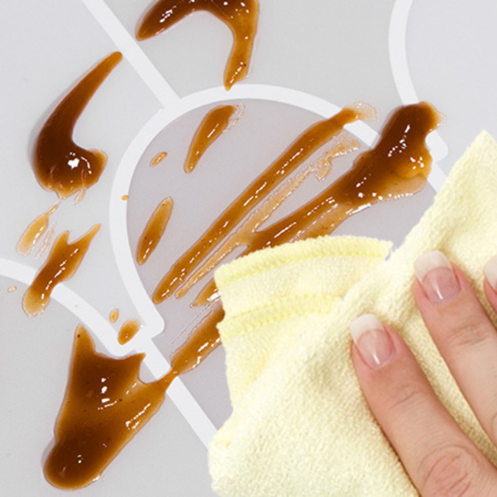 Person cleaning a grey tile with caramel residue using a yellow cloth on a white background