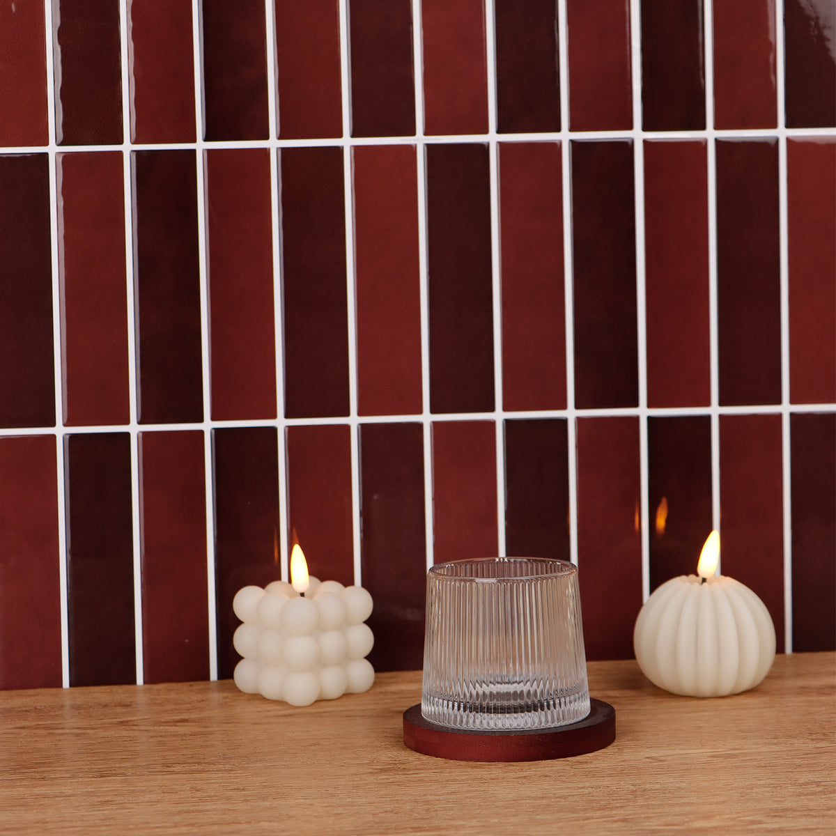 Two lit candles and a glass on a wooden surface with a tiled wall background