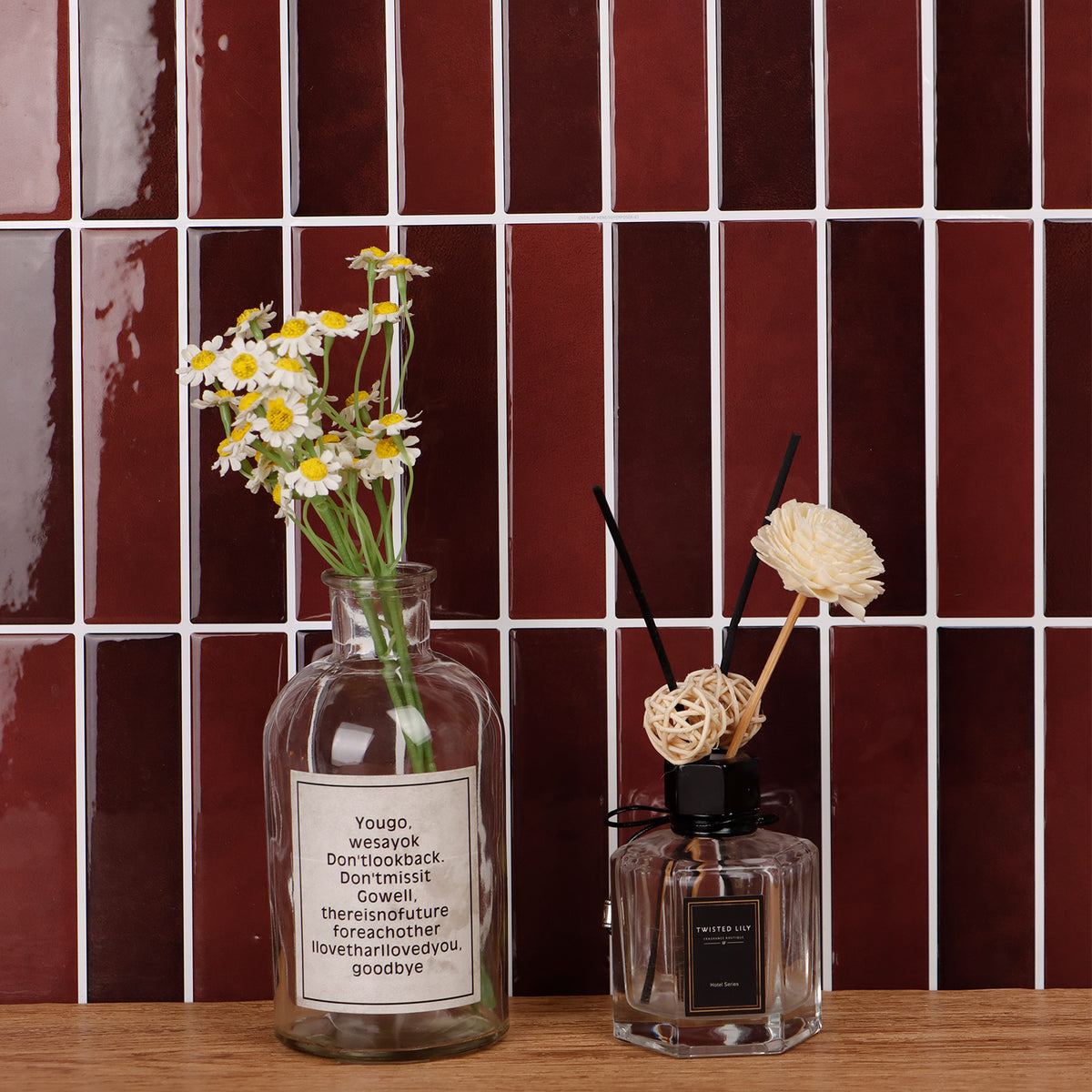 Two decorative bottles with flowers against a red tiled wall.