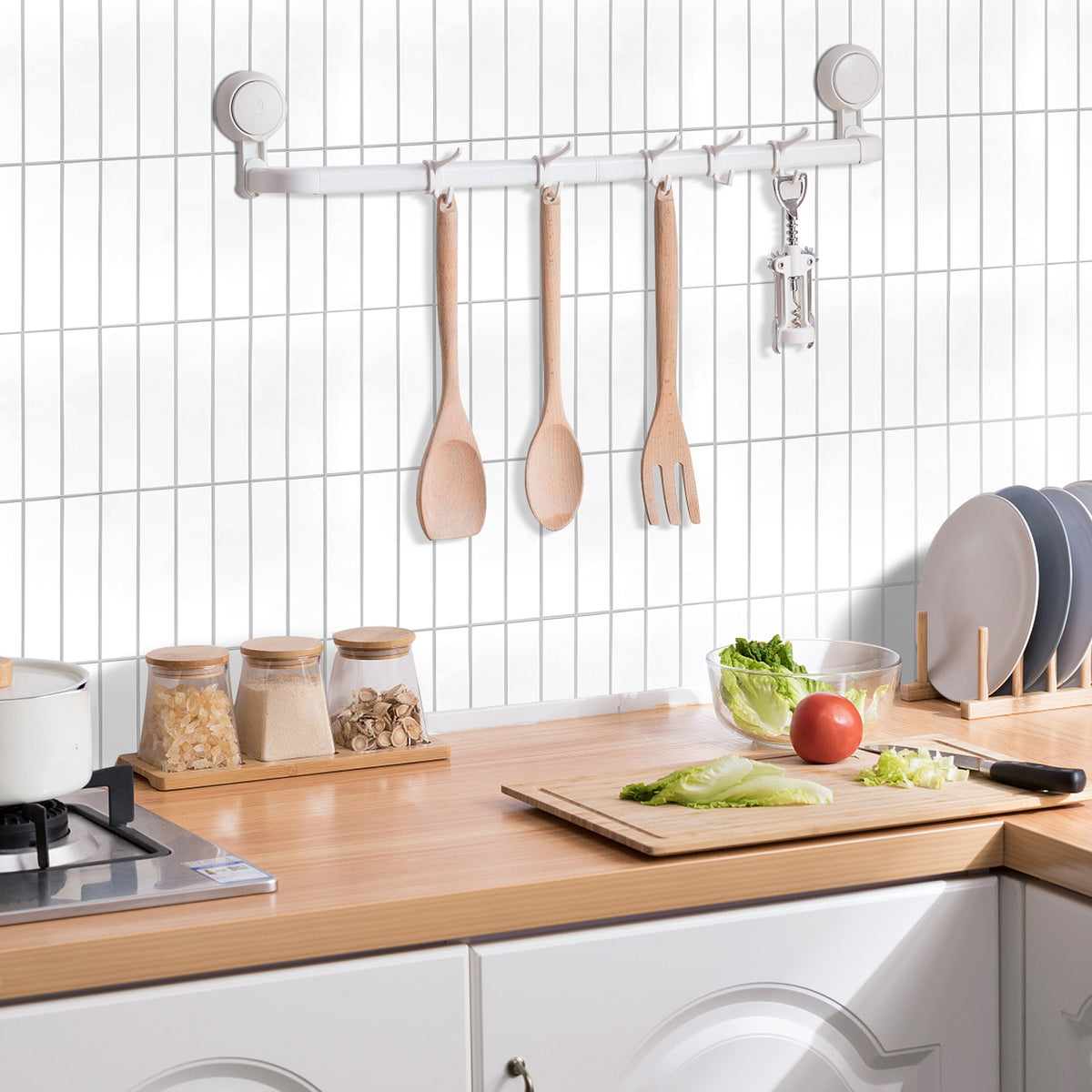 Kitchen counter with utensils hanging on a rack against a tiled wall.