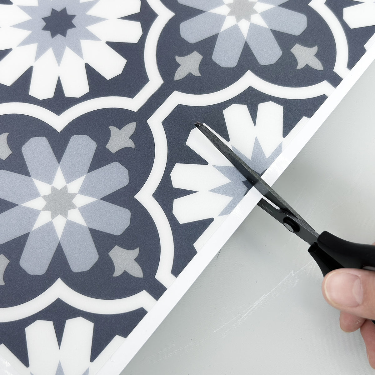Person cutting a decorative tile with scissors on a matching patterned surface.