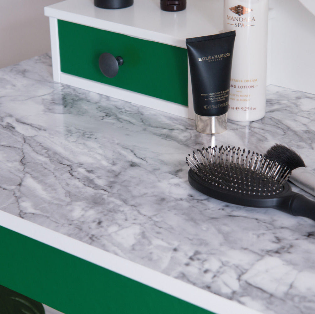 Hairbrush and hair products on a marble countertop with a green drawer.