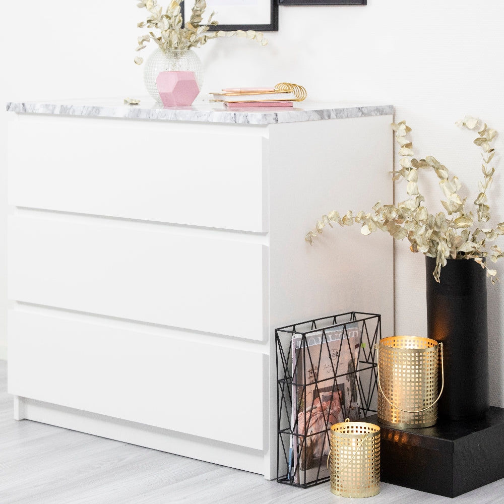 White dresser with decorative items including a black vase, gold candle holder, and white flowers on a light gray floor.
