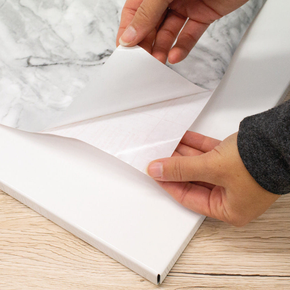 Person unrolling marble adhesive vinyl on a wooden surface