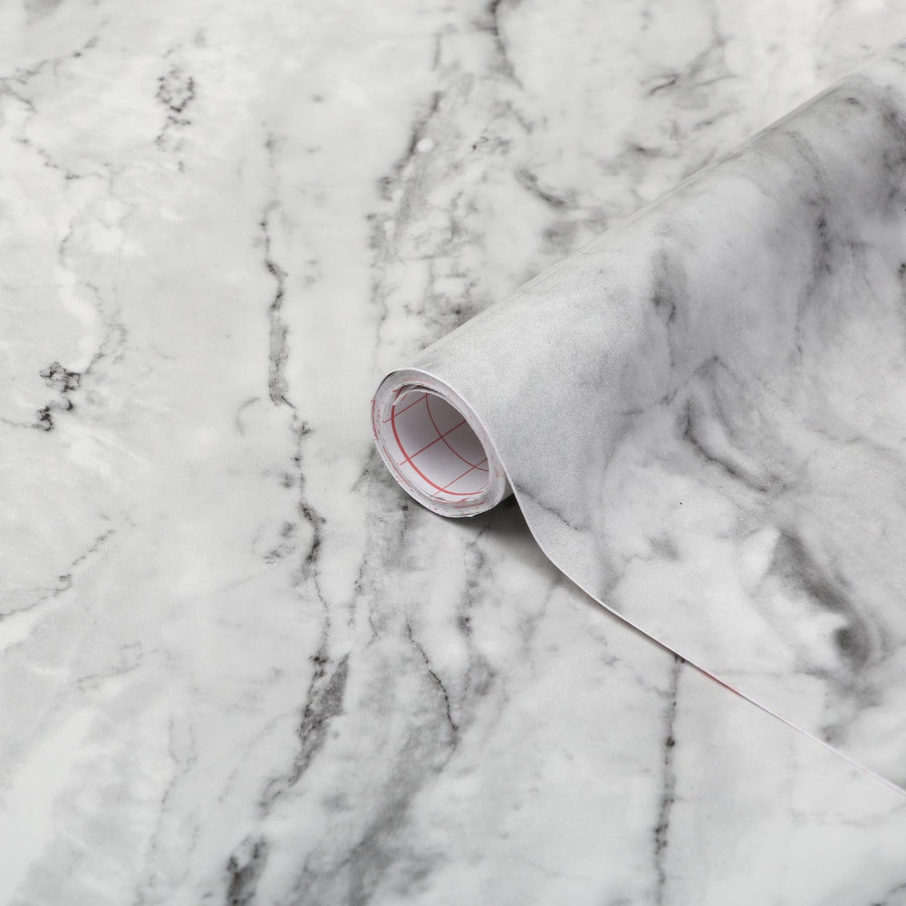 Decorative vase with gold leaves on a marble surface with a pink geometric cup and notebook.