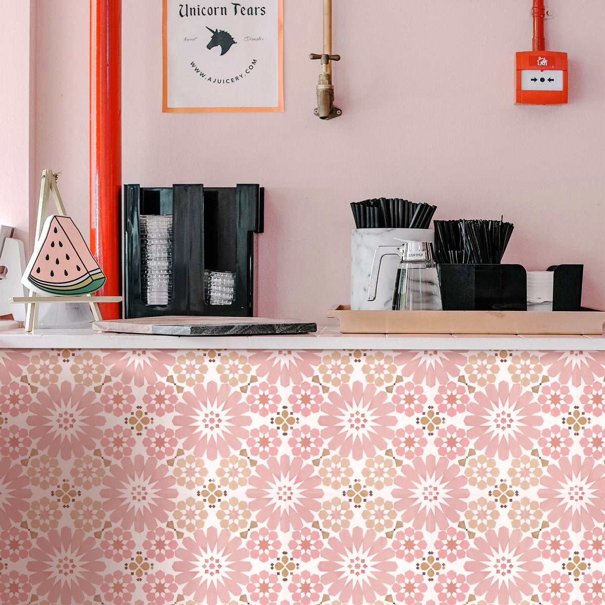 Coffee station with coffee-making equipment against a pink wall with a floral patterned base.