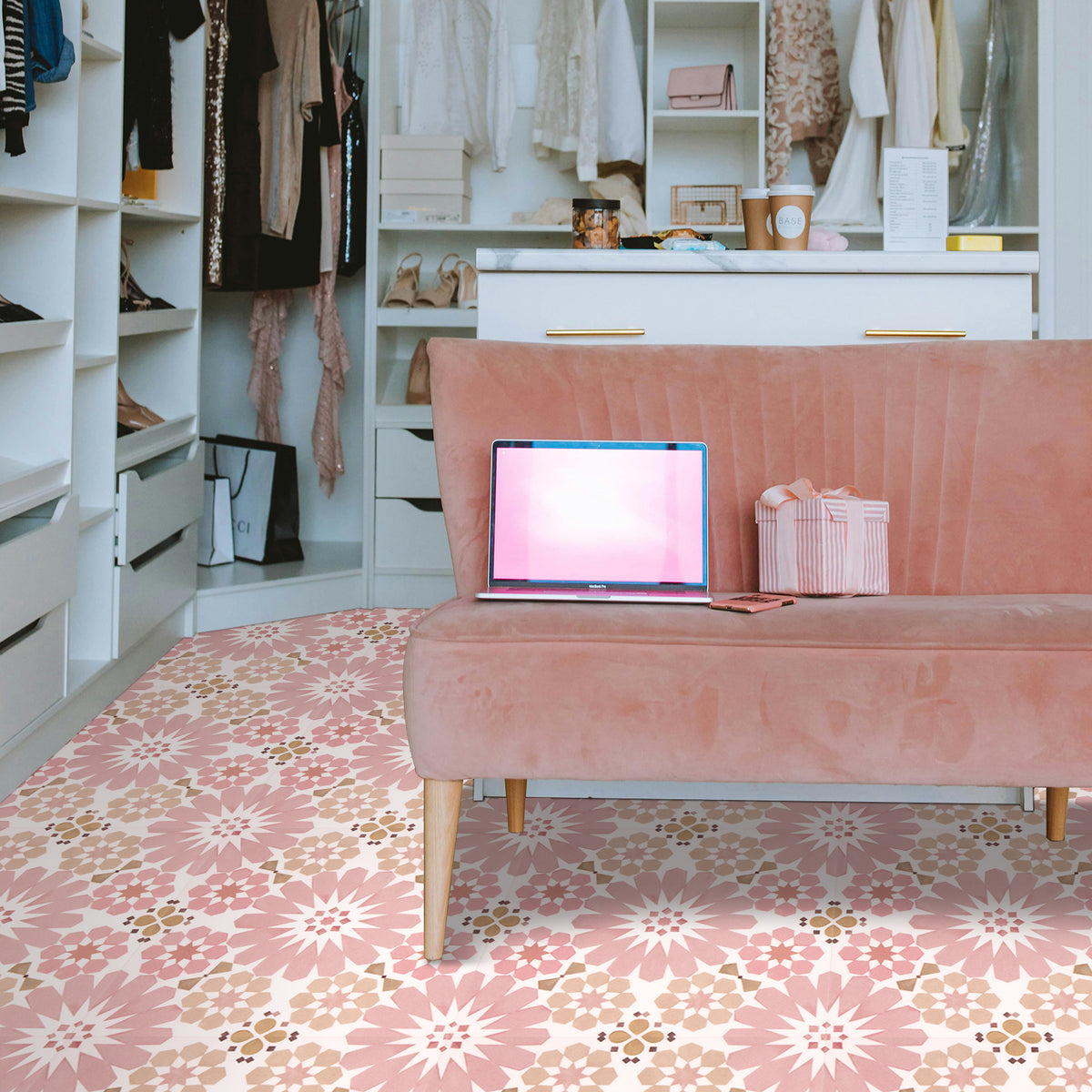 Pink sofa with a laptop on it in a room with shelves and a floral floor tiles.