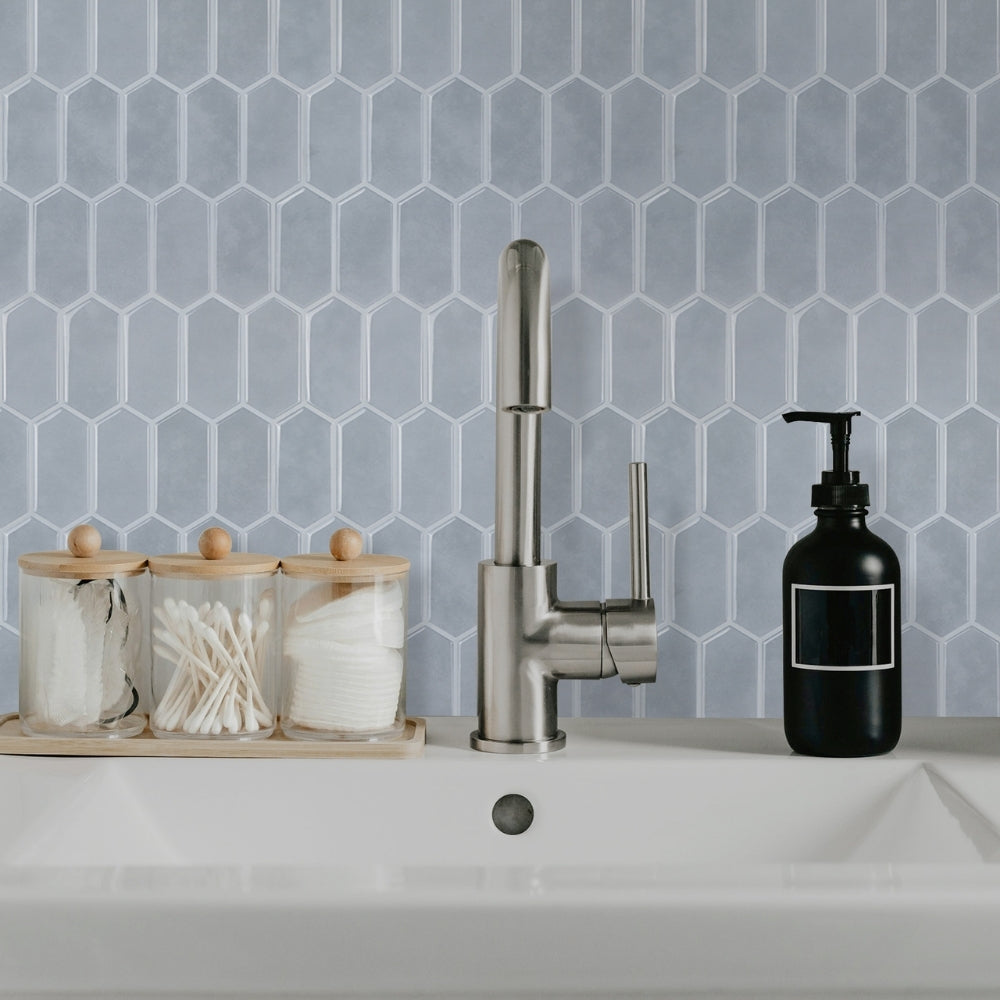 Kitchen sink with faucet, soap dispenser, and cleaning supplies against a blue hexagonal tile backsplash.