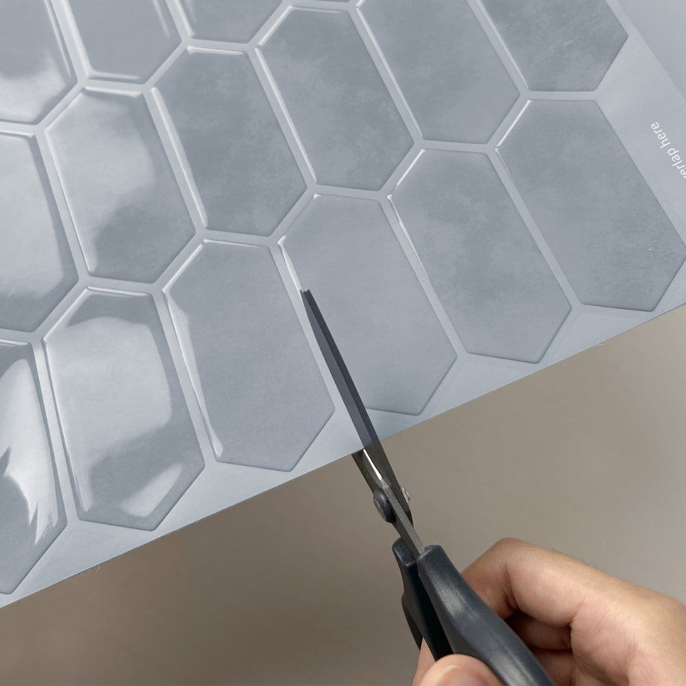 Hexagonal tiles with a hand holding scissors, likely for cutting or applying the tiles.