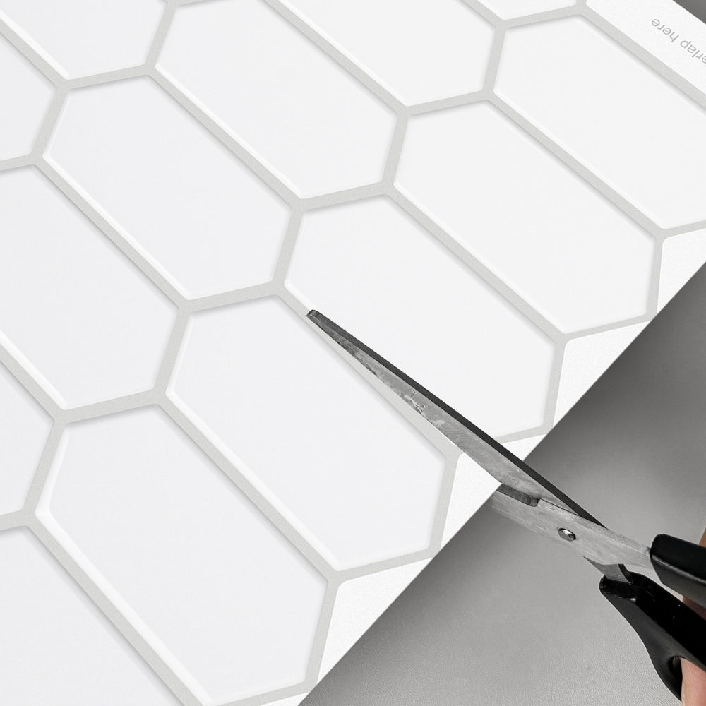 Person cutting a hexagonal tile with scissors on a white background