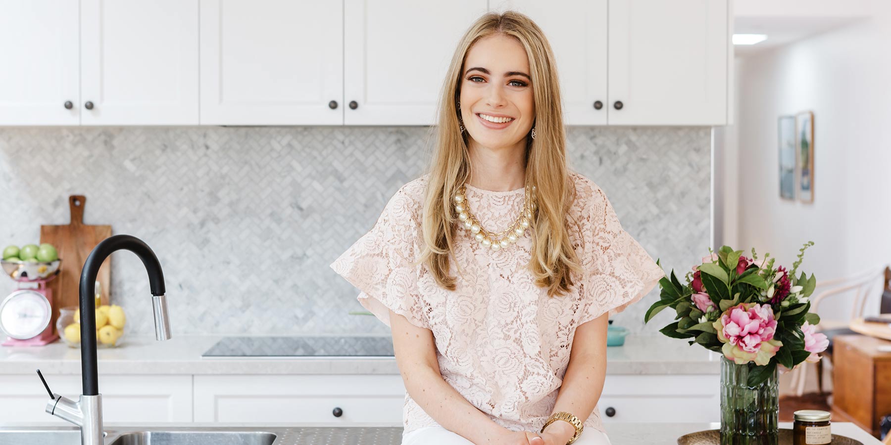 young woman with blonde long hair and pink top in front of white kitchen cupboards - professionals